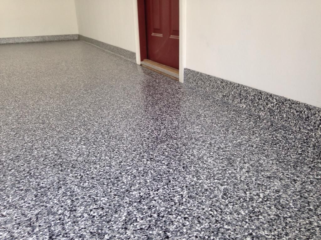 Empty room with speckled gray floor and white walls, showing a closed red door.