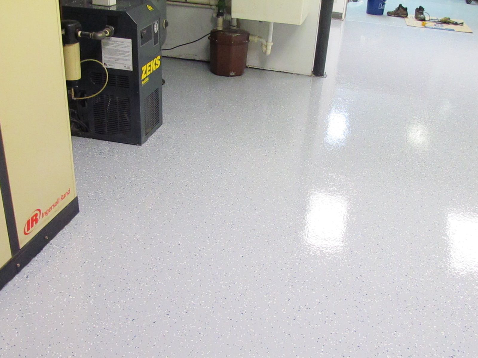 Empty glossy hallway with speckled floor, a trash can, and office equipment along the wall