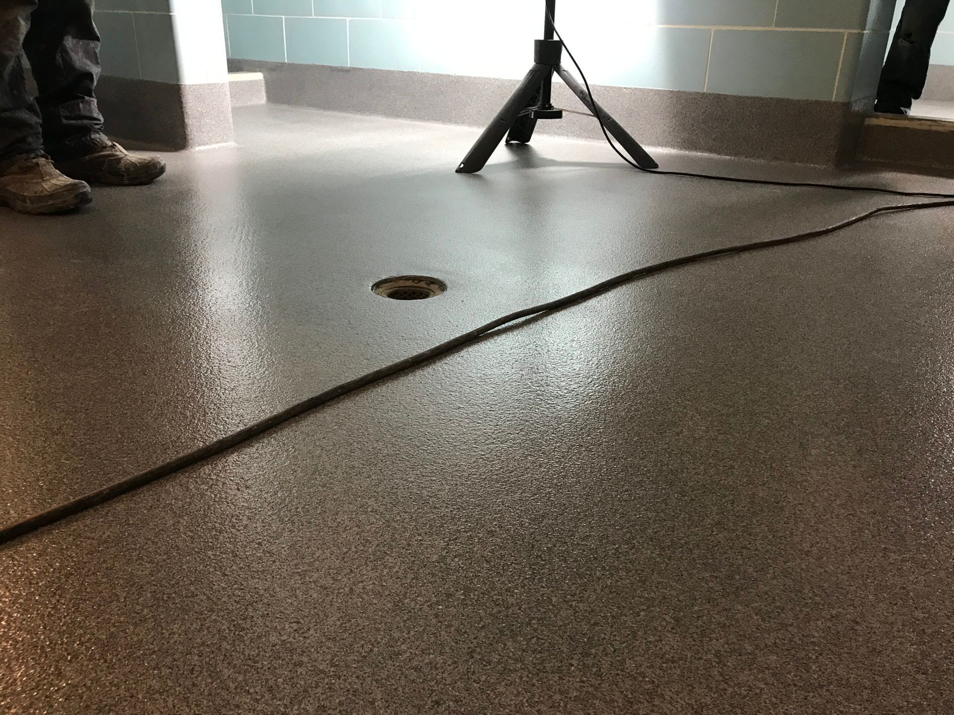 Tripod in a tiled room with a black cable across the floor and a person’s boots at left