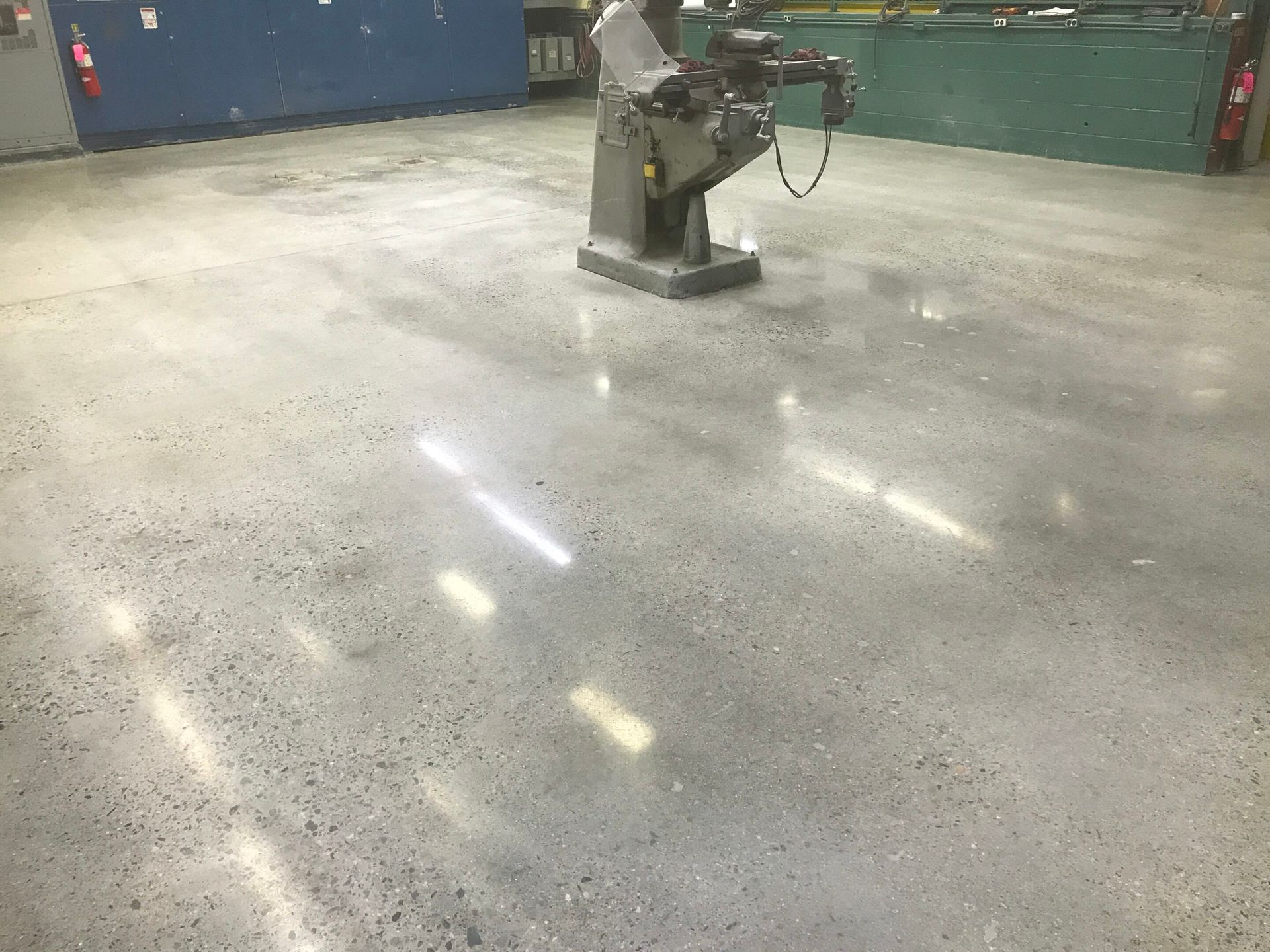 Industrial floor with a polished concrete surface and a machine near blue and green equipment cabinets.