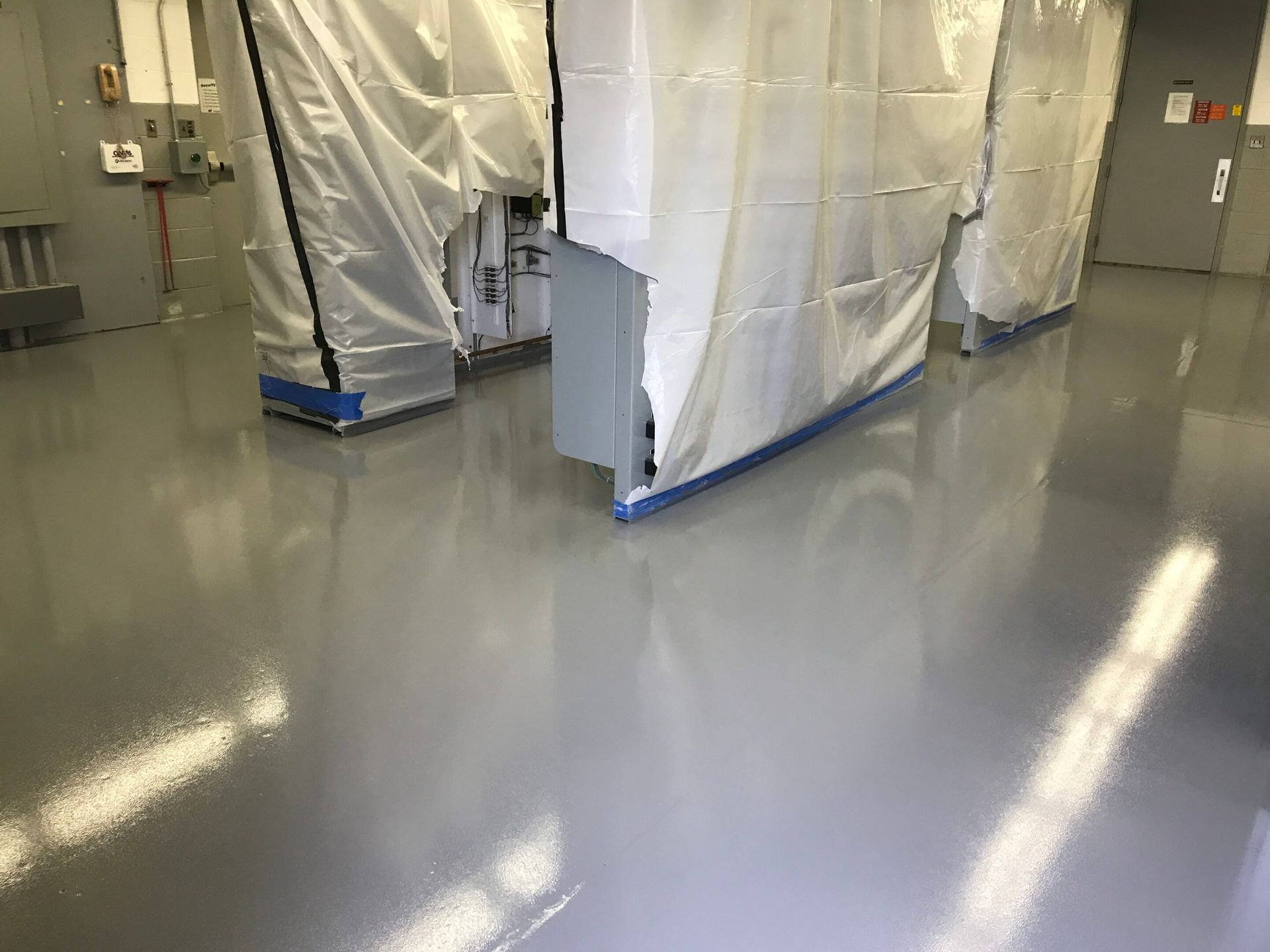 Plastic-wrapped industrial equipment in a clean room with a glossy gray floor