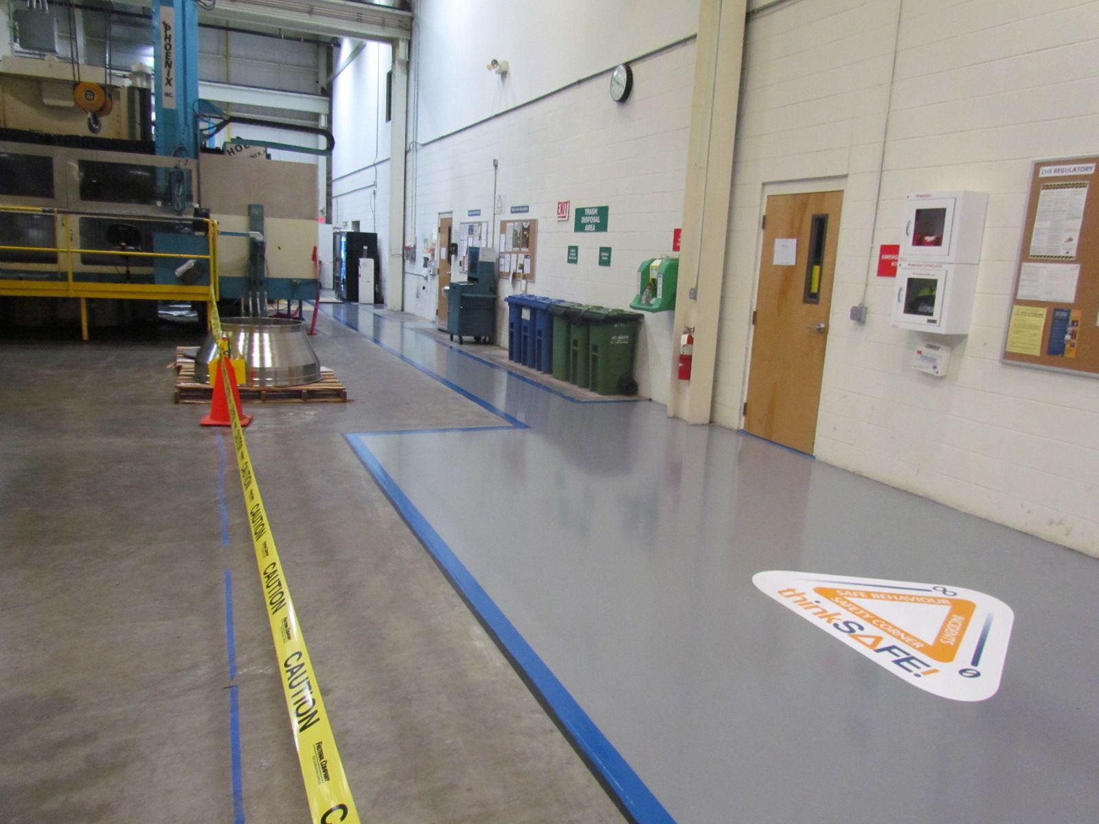 Warehouse aisle with yellow caution tape, orange cones, and blue floor markings beside a loading area