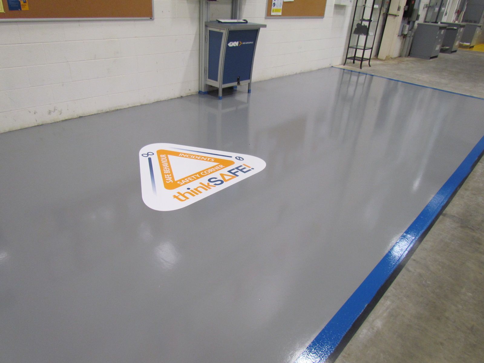 Industrial floor with a gray coating and a triangular warning sign, next to a blue line in a warehouse-like space