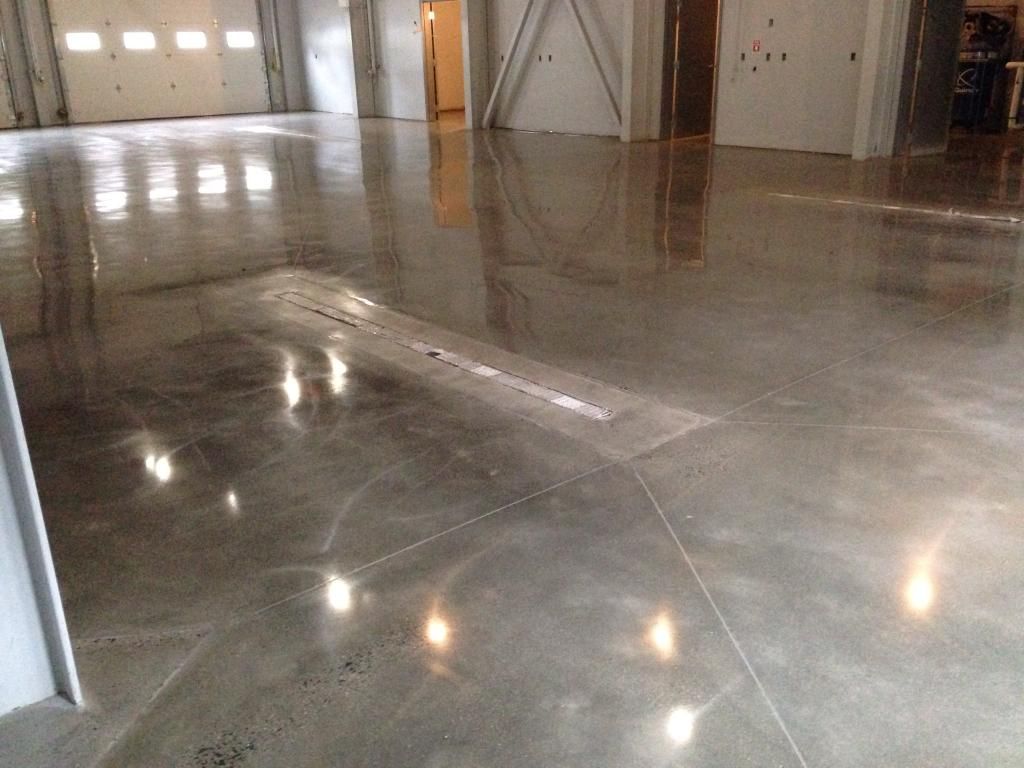 Polished concrete floor in a large empty warehouse with reflected lights and garage doors