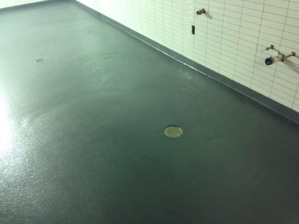 Empty green-tiled shower room with floor drains and wall-mounted faucets