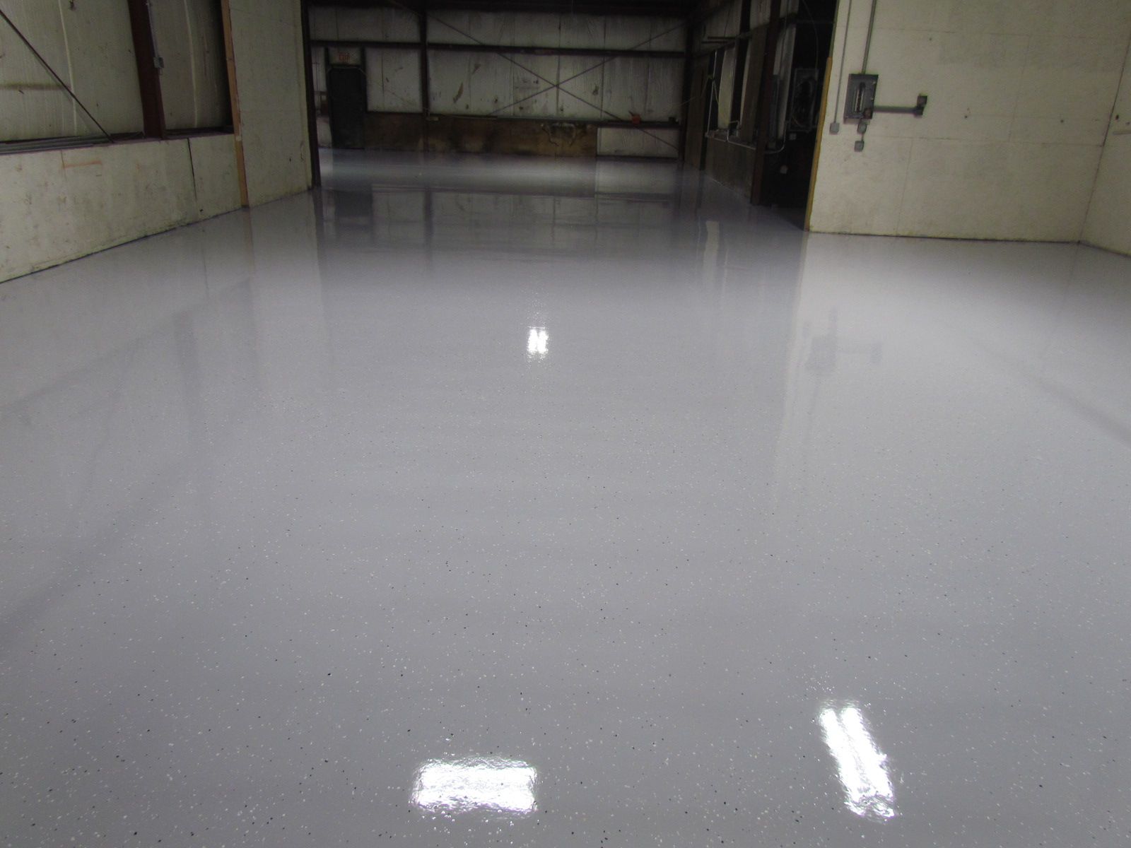 Empty indoor warehouse with a glossy white floor and overhead light reflections