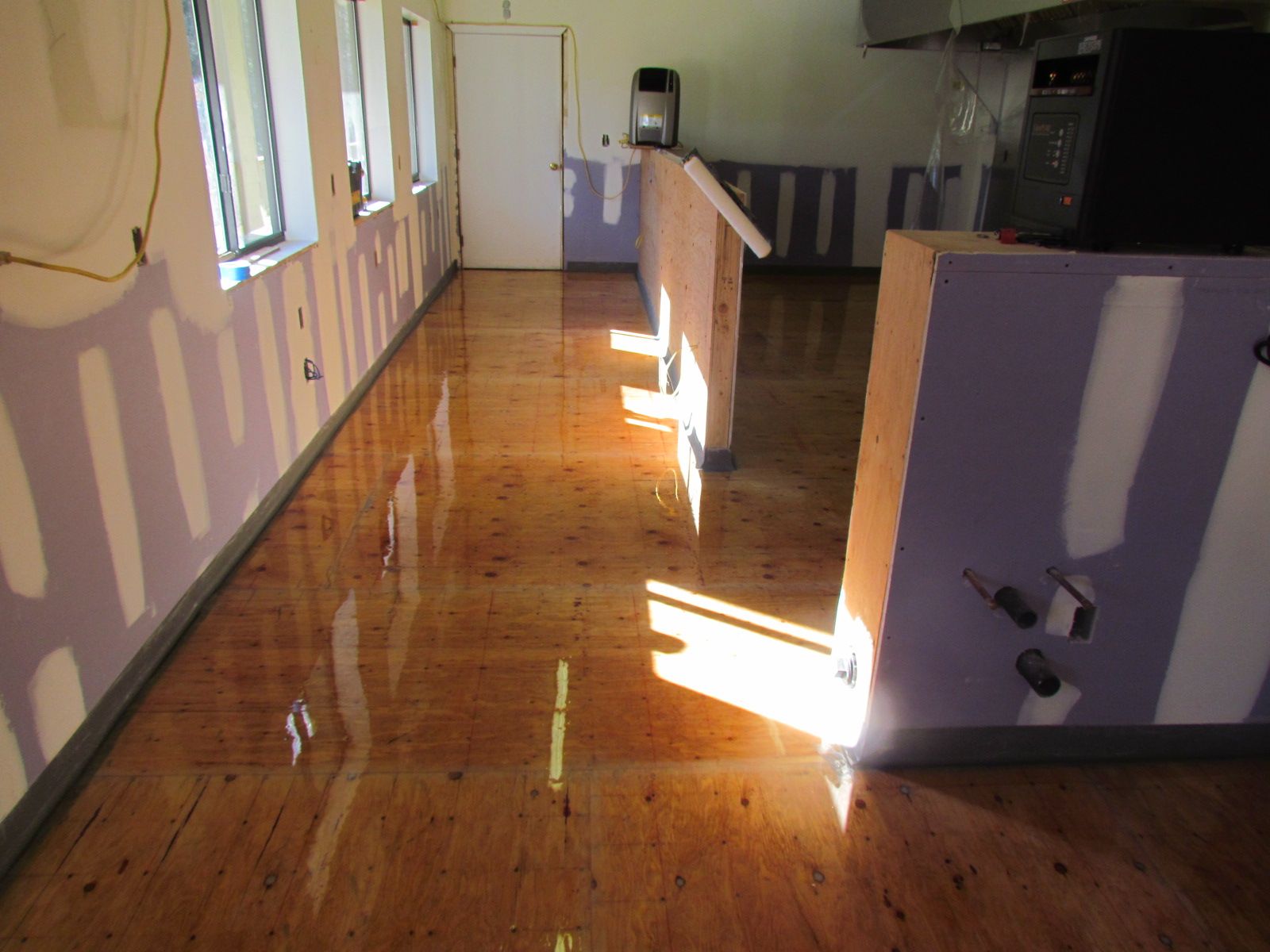 Empty room with polished wooden floor, purple walls, and bright sunlight streaming through windows.