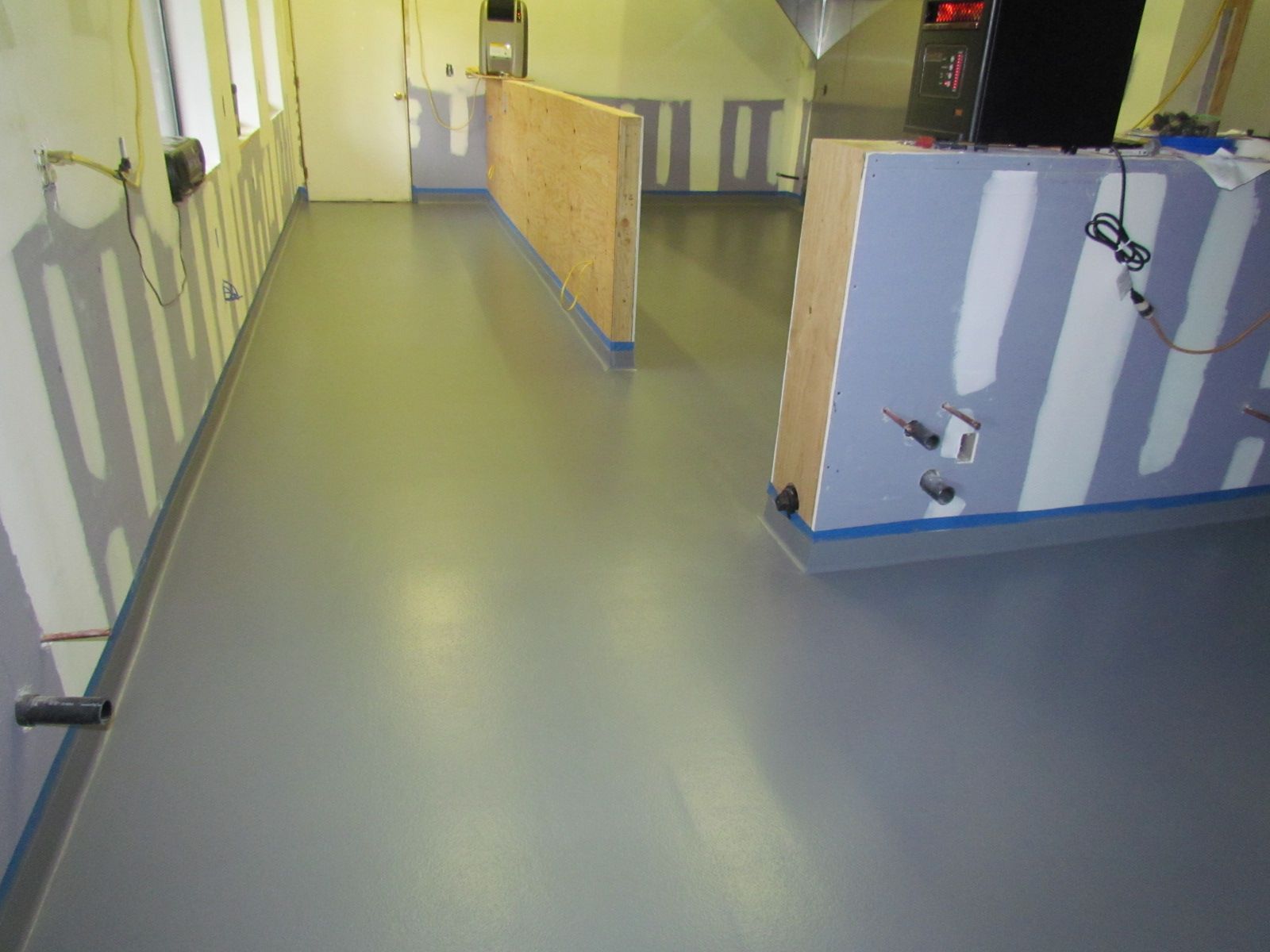 Empty indoor hallway with yellow walls and gray floor, lined with countertops and cabinets
