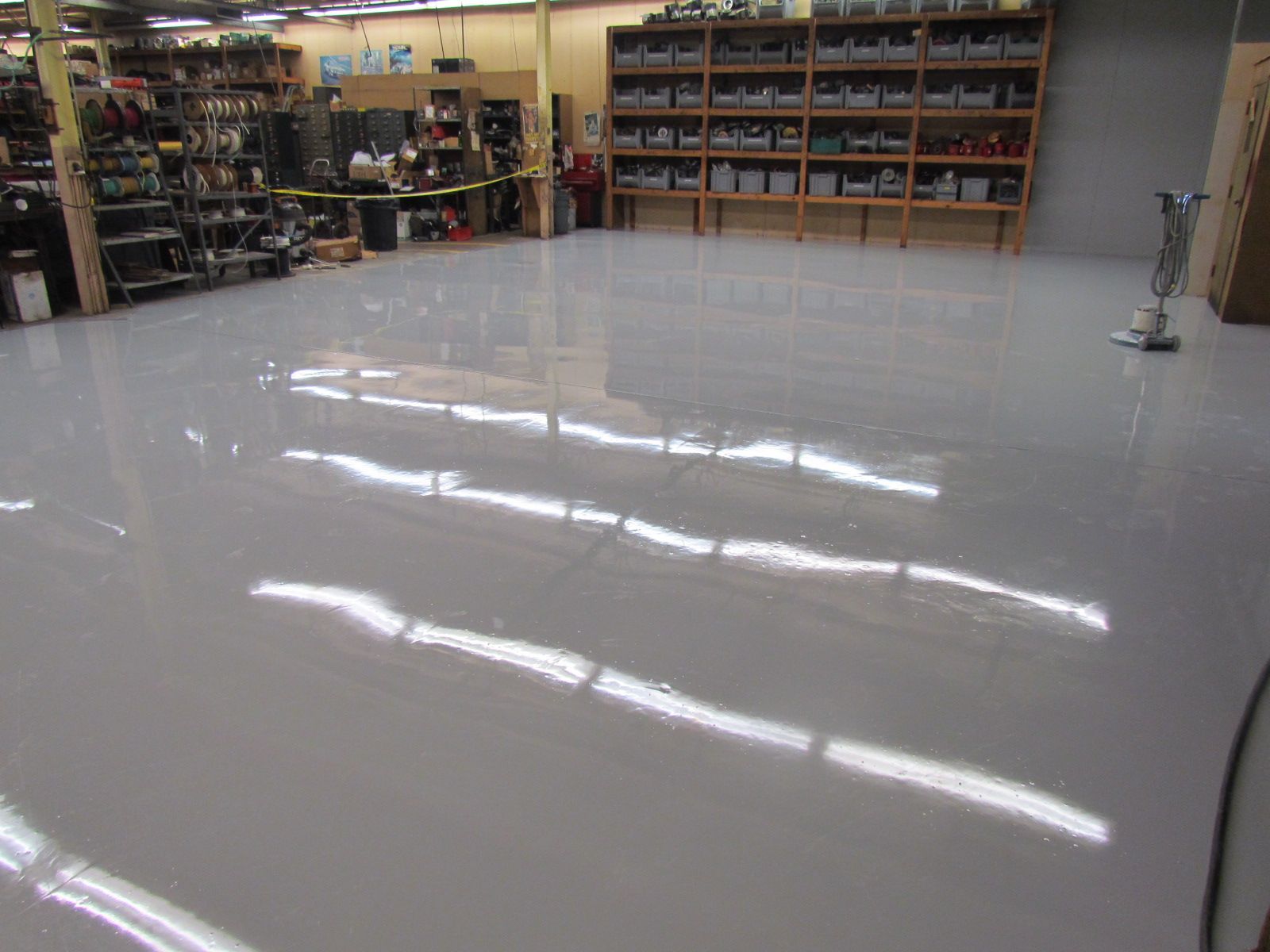 Empty glossy white showroom floor with shelves and tools along the back wall