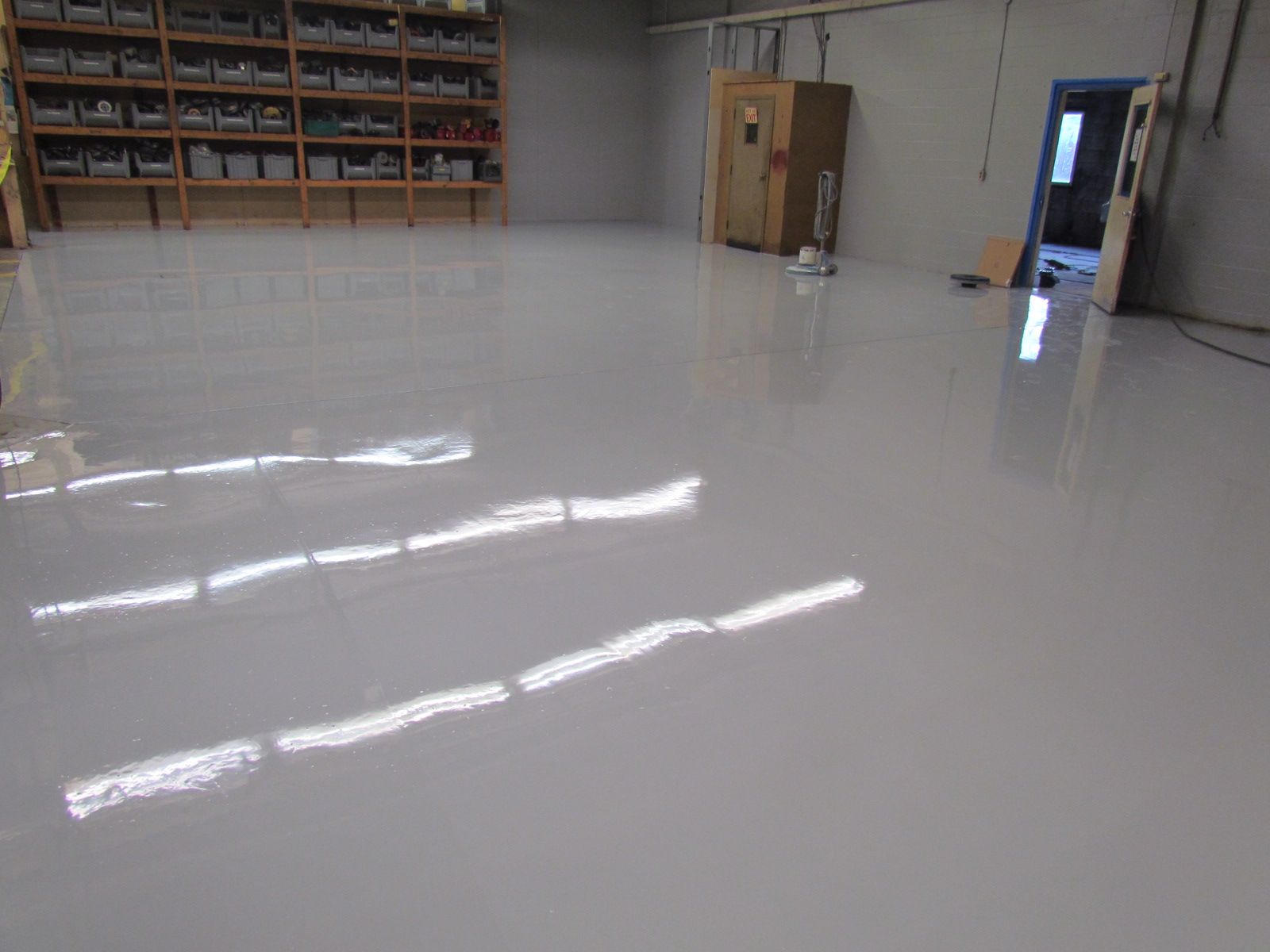 Empty glossy warehouse floor with reflections, shelves along the wall, and an open door at right
