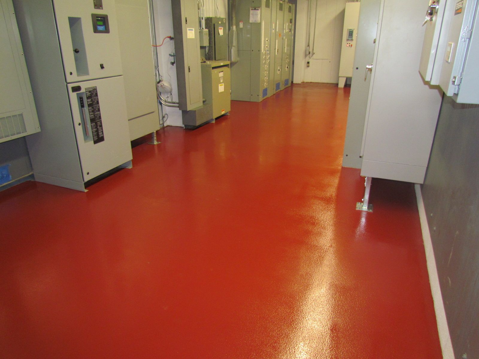 Empty industrial hallway with a glossy red floor and electrical cabinets along the walls