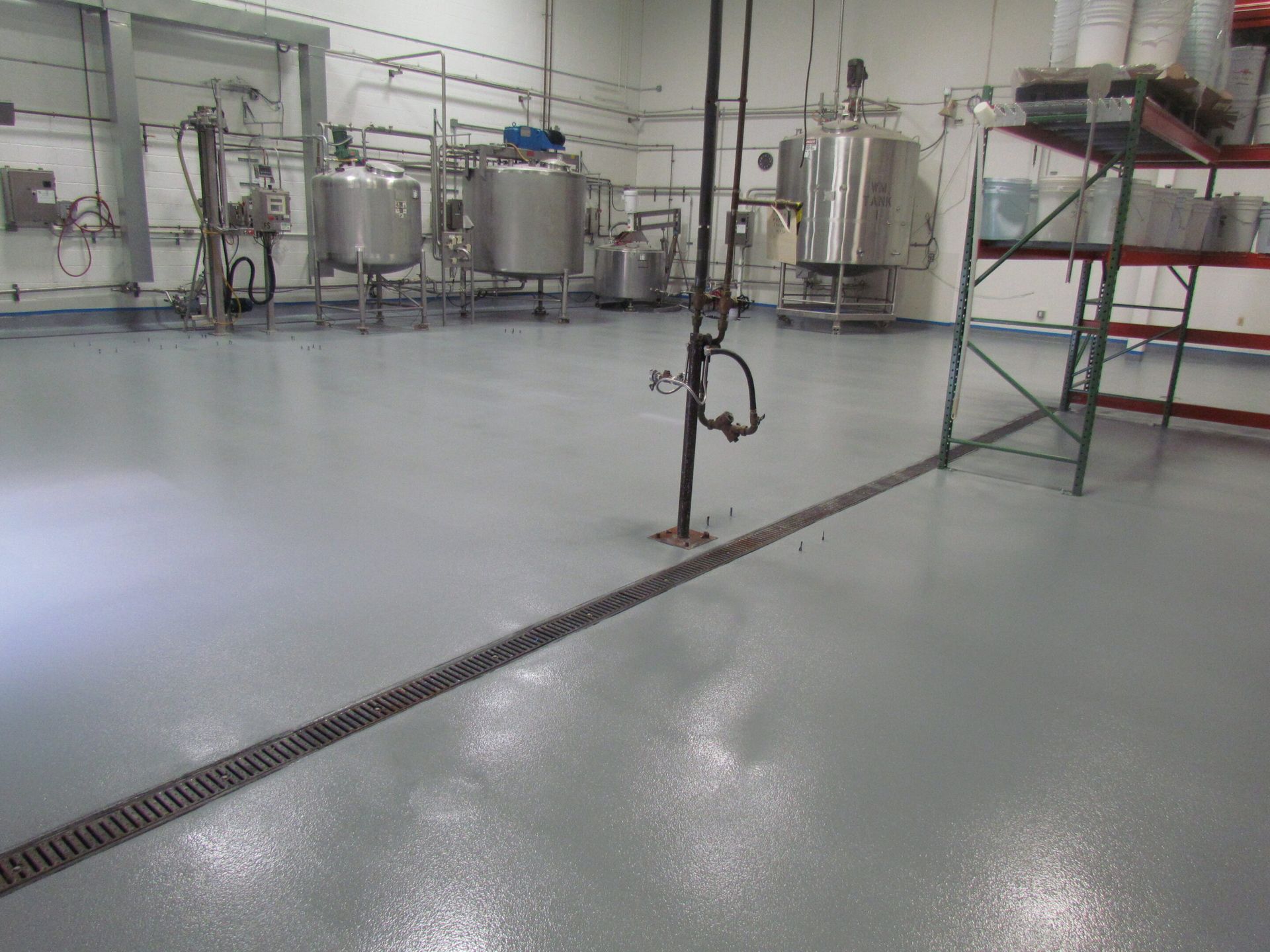 Empty industrial room with stainless steel tanks, piping, and a gray epoxy floor