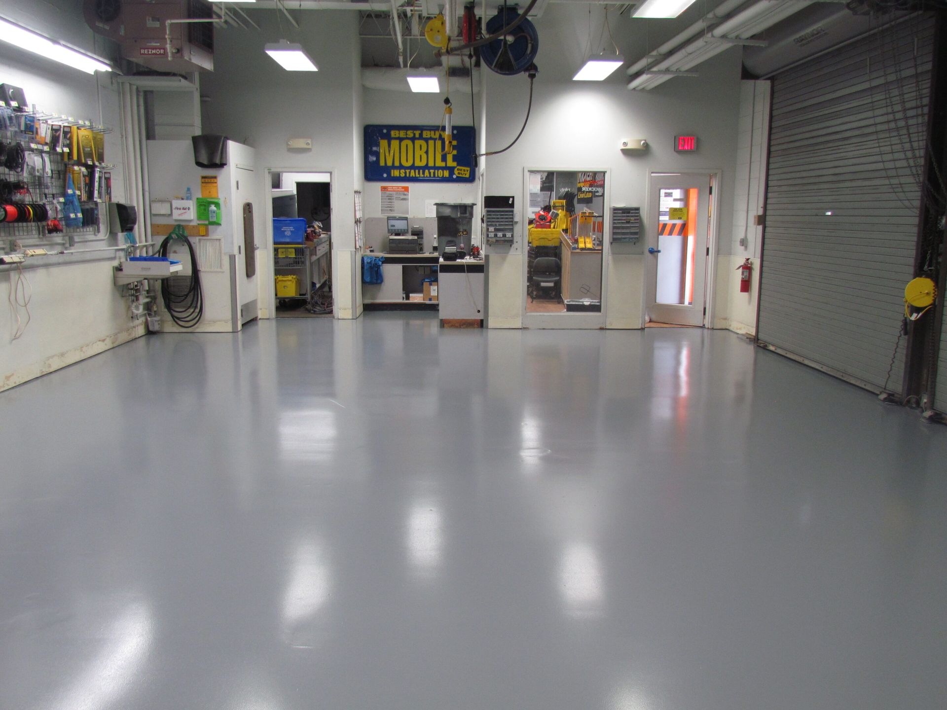 Empty auto repair shop with a gray floor, tool displays, and a closed garage door
