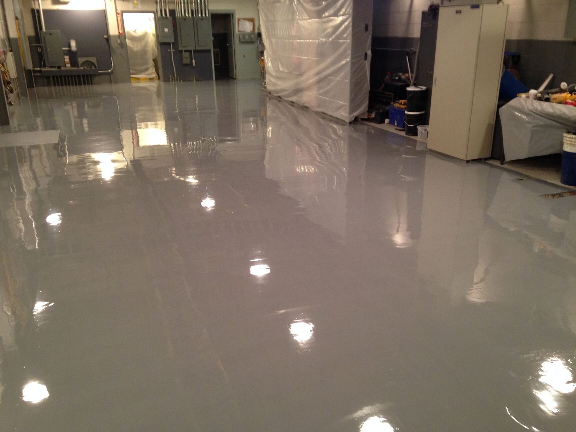 Empty glossy gray floor in a large indoor room with equipment along the walls