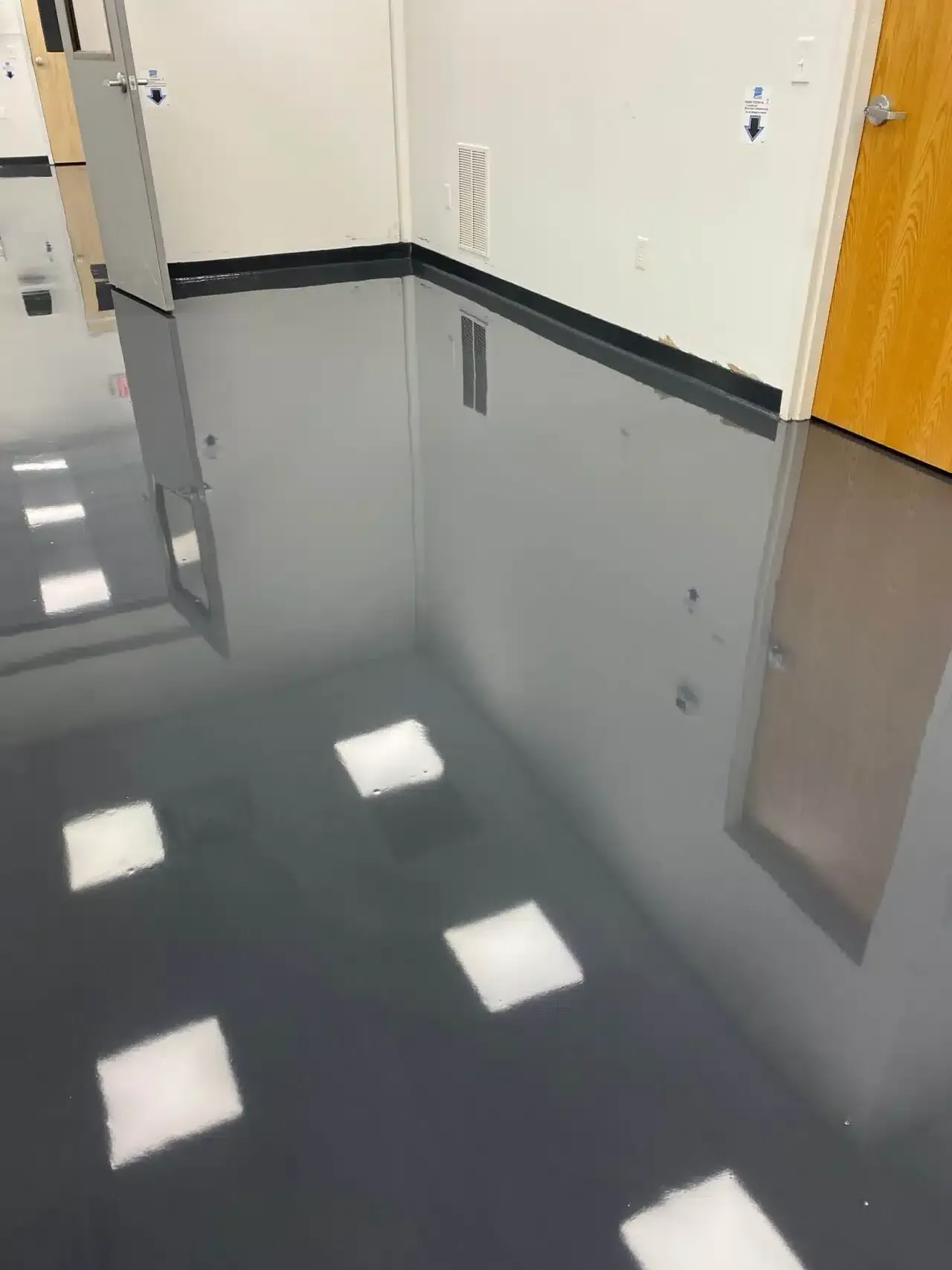 Flooded hallway with reflective water, white floor tiles, and a yellow door along the right wall.
