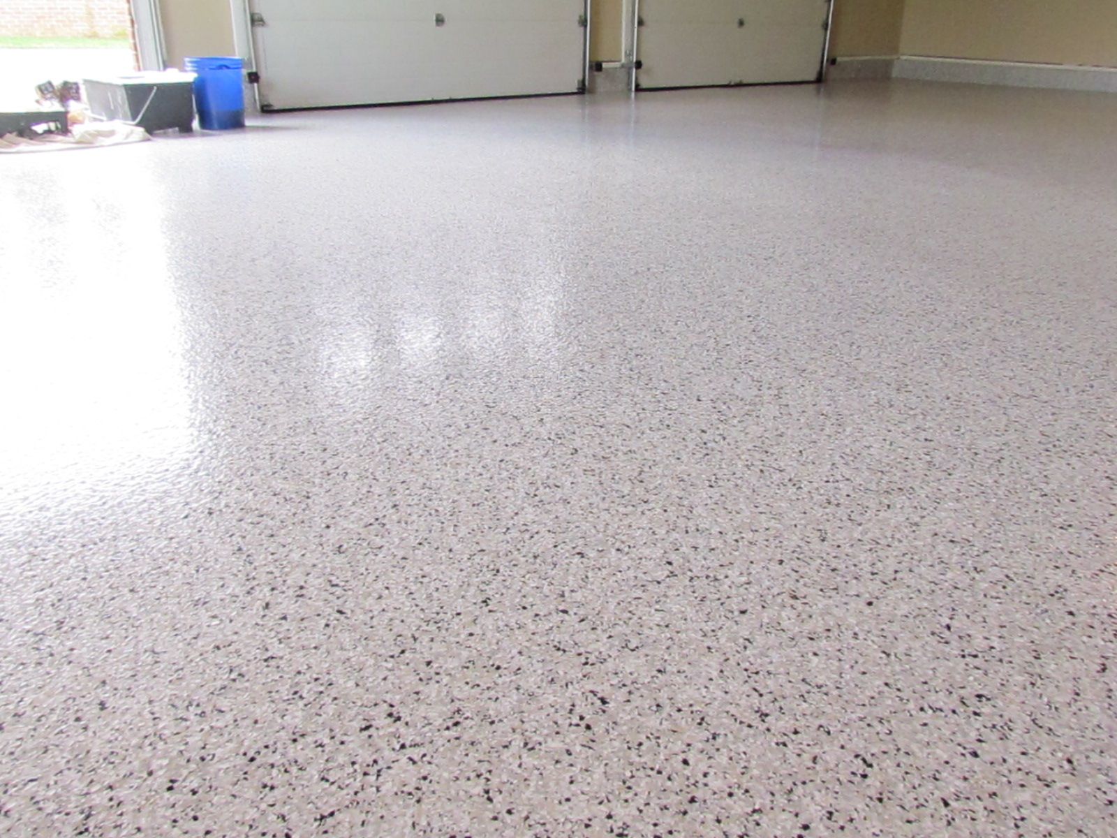 Empty speckled floor in a bright indoor room with cabinets and a blue bin in the background