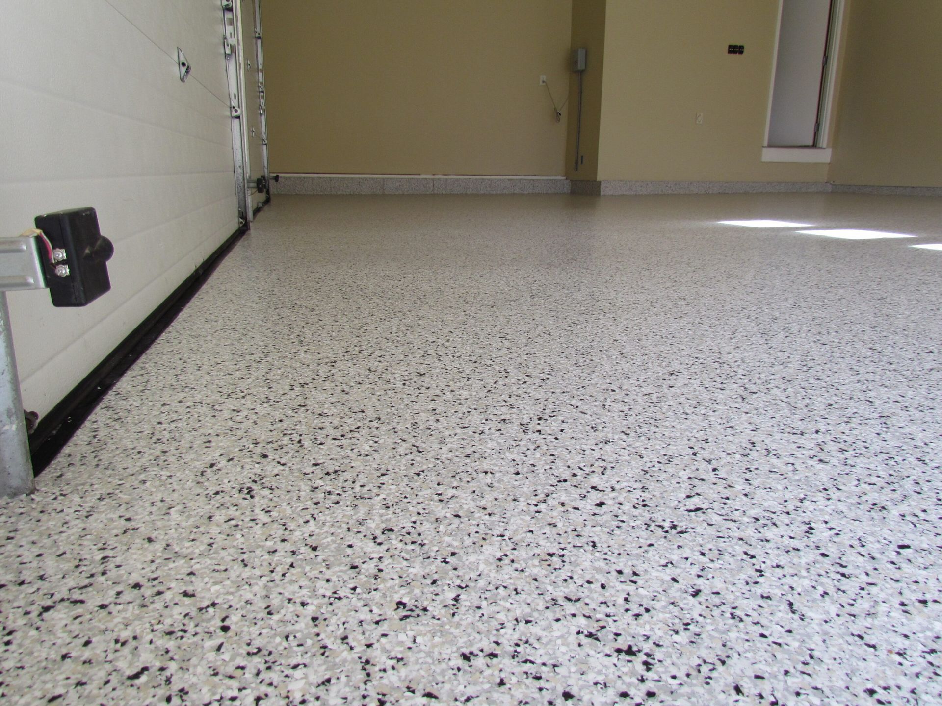 Empty speckled floor in a plain room with beige walls and bright light from the right