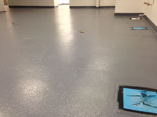 Empty gray floor in a hallway with a few blue mats near the walls.