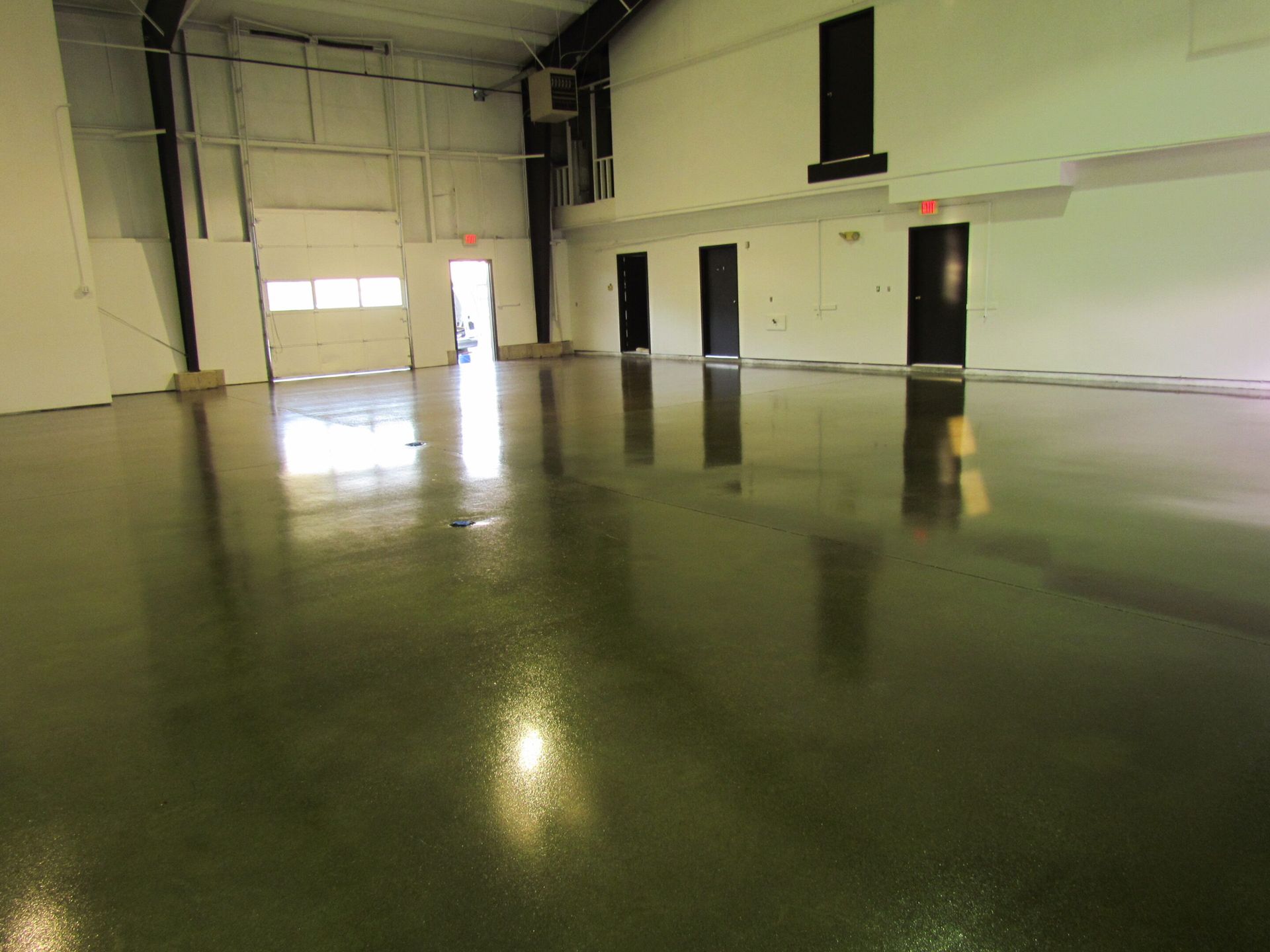 Empty indoor warehouse with polished concrete floor and tall doors along the wall