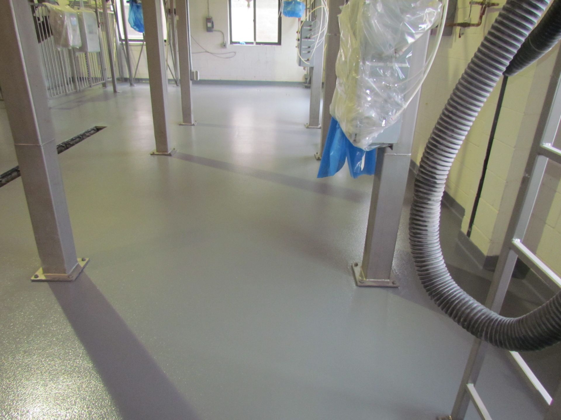 Empty industrial hallway with gray floor, metal posts, and a large flexible hose on the right