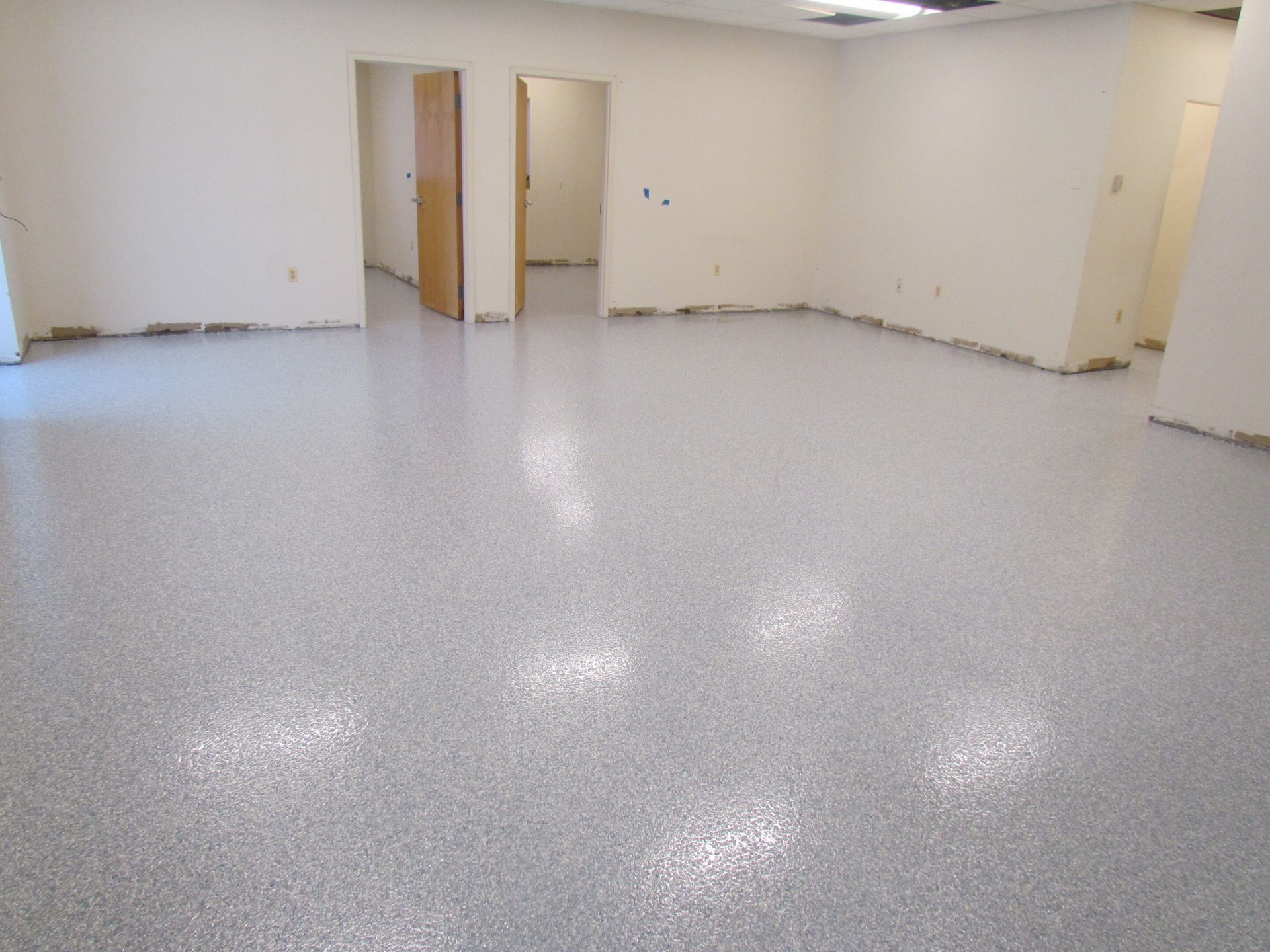 Empty white room with gray speckled floor and several open doorways