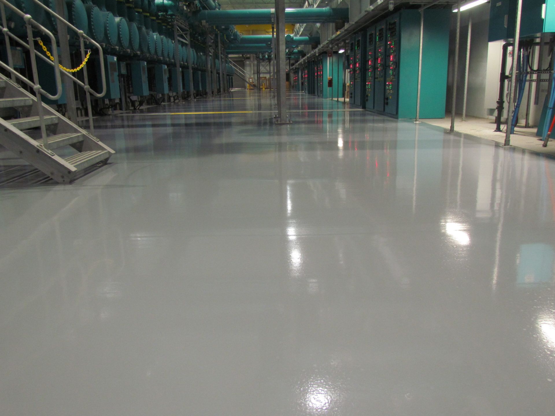 Empty industrial hallway with a glossy floor and teal walls under overhead lights