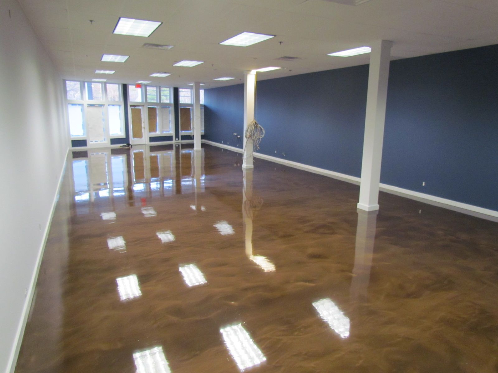Empty office space with polished wood floor, blue walls, white columns, and glass doors at the back.