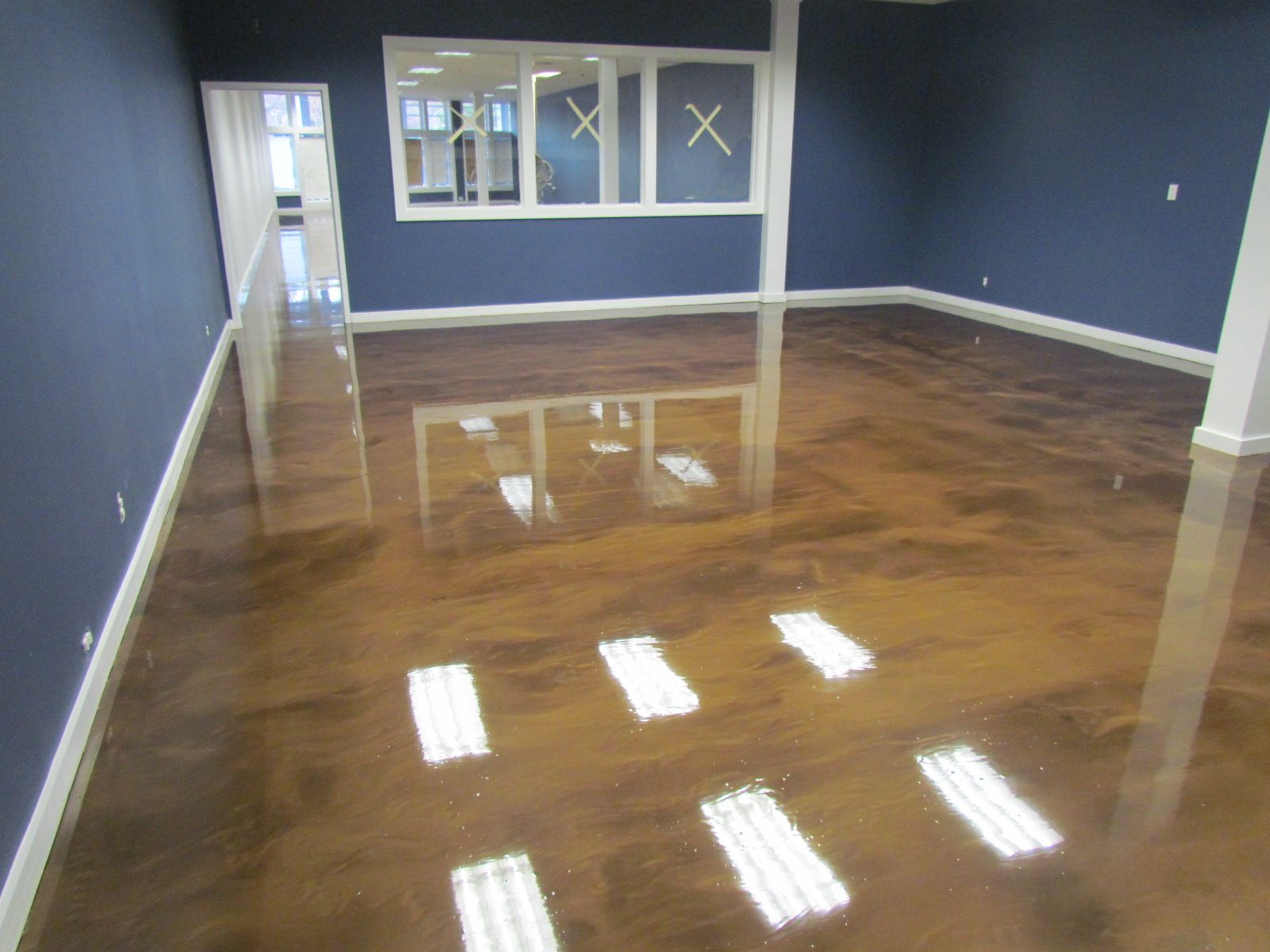 Empty room with glossy wood floor, blue walls, and windows reflecting light