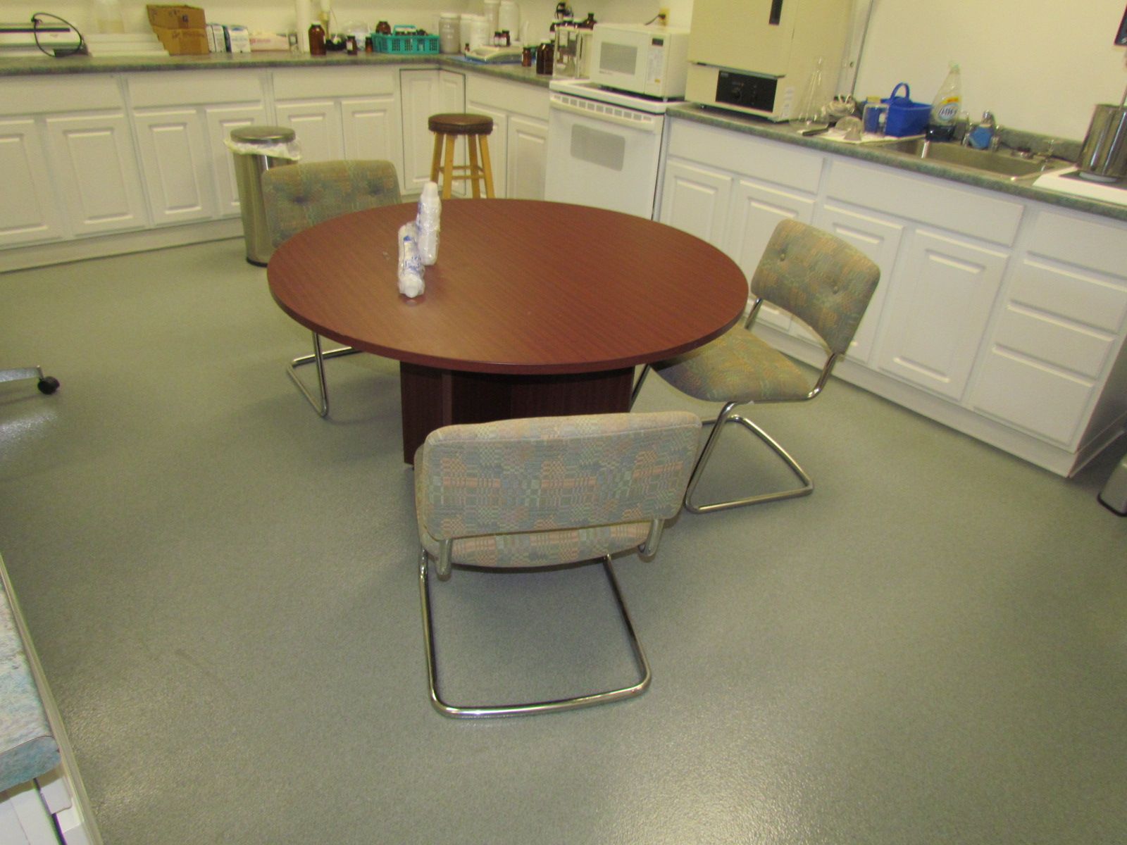 Small office break room with a round table, three chairs, white cabinets, and a sink.