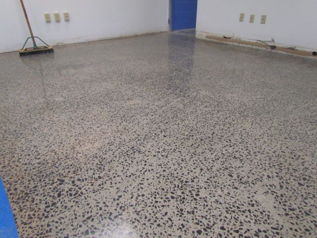 Empty room with speckled tile floor, white walls, and a broom in the corner