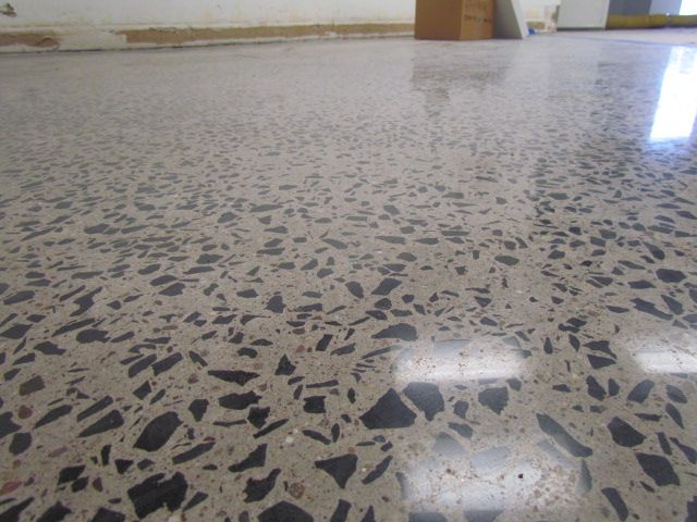 Polished terrazzo floor with dark speckles reflecting overhead lights in an indoor hallway.