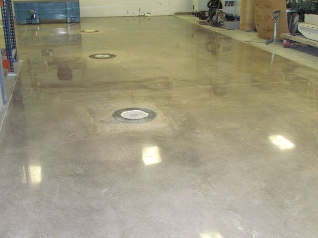 Empty glossy concrete floor in a warehouse or garage with floor drains and reflected lights