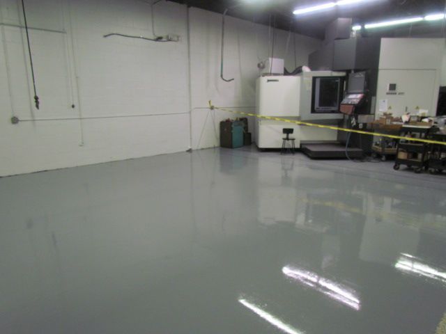 Empty industrial workshop with gray polished floor, white walls, and machinery along the right side.