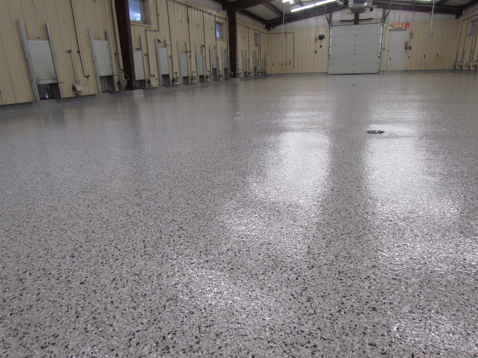 Empty indoor warehouse with a polished speckled floor and closed doors along the walls
