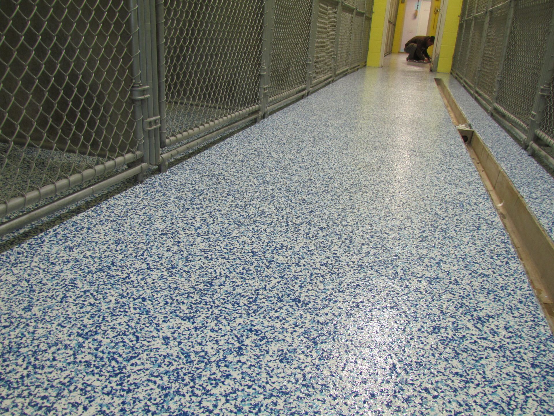 Speckled blue floor in a fenced corridor with a yellow door at the far end