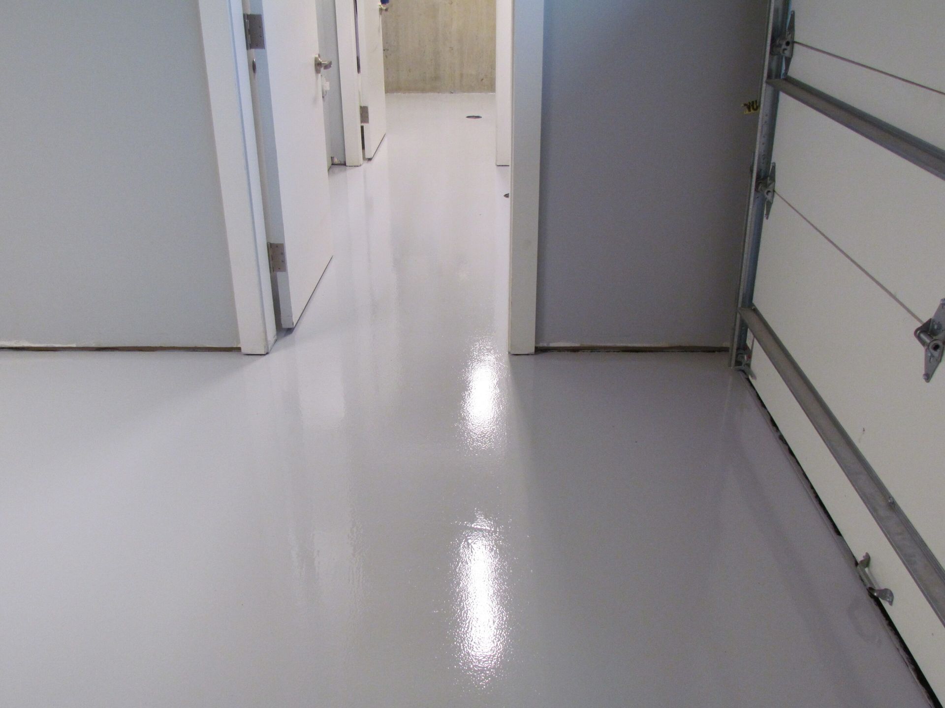 Empty white garage with glossy floor and open doorway to a hallway