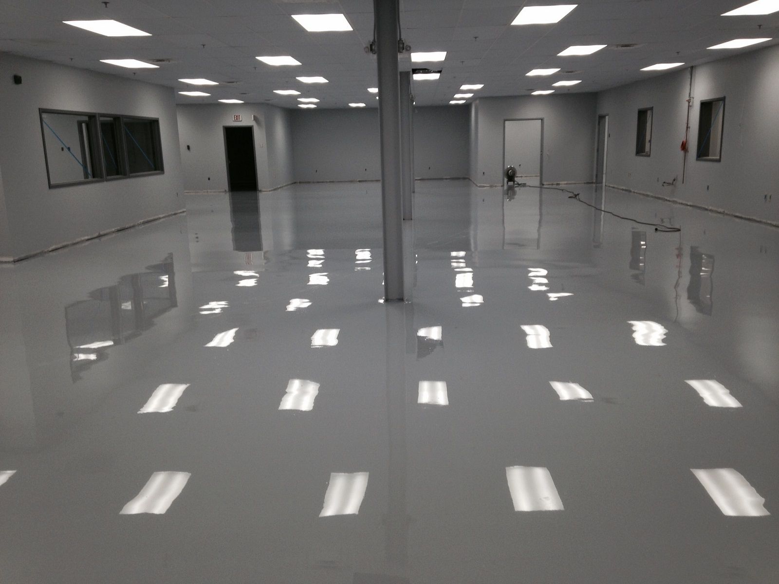 Empty gray indoor room with glossy floor, ceiling lights, and windows along the walls