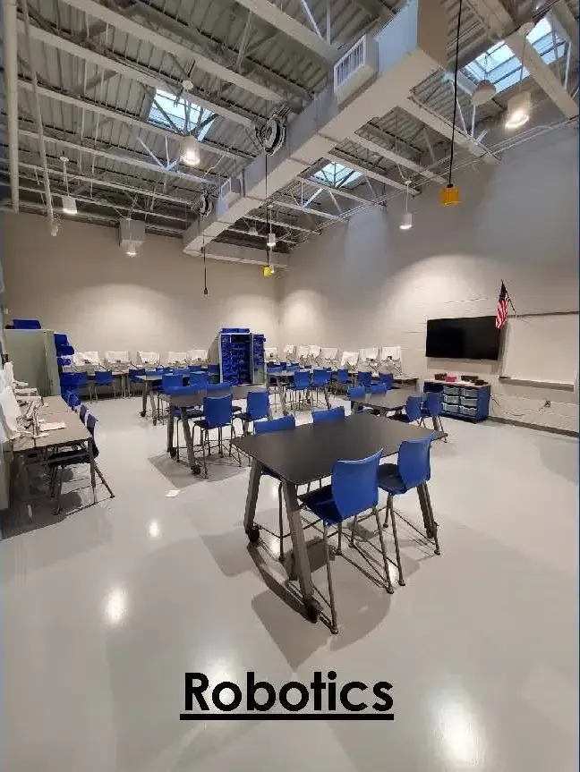 Spacious robotics classroom with blue chairs, lab tables, and industrial ceiling lights