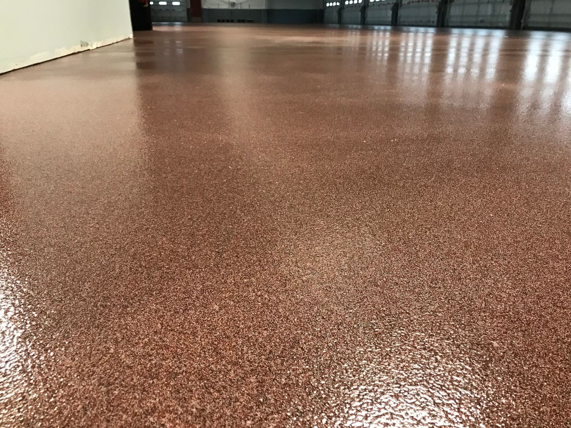 Glossy reddish-brown speckled floor in a hallway or lobby, with doors in the distance