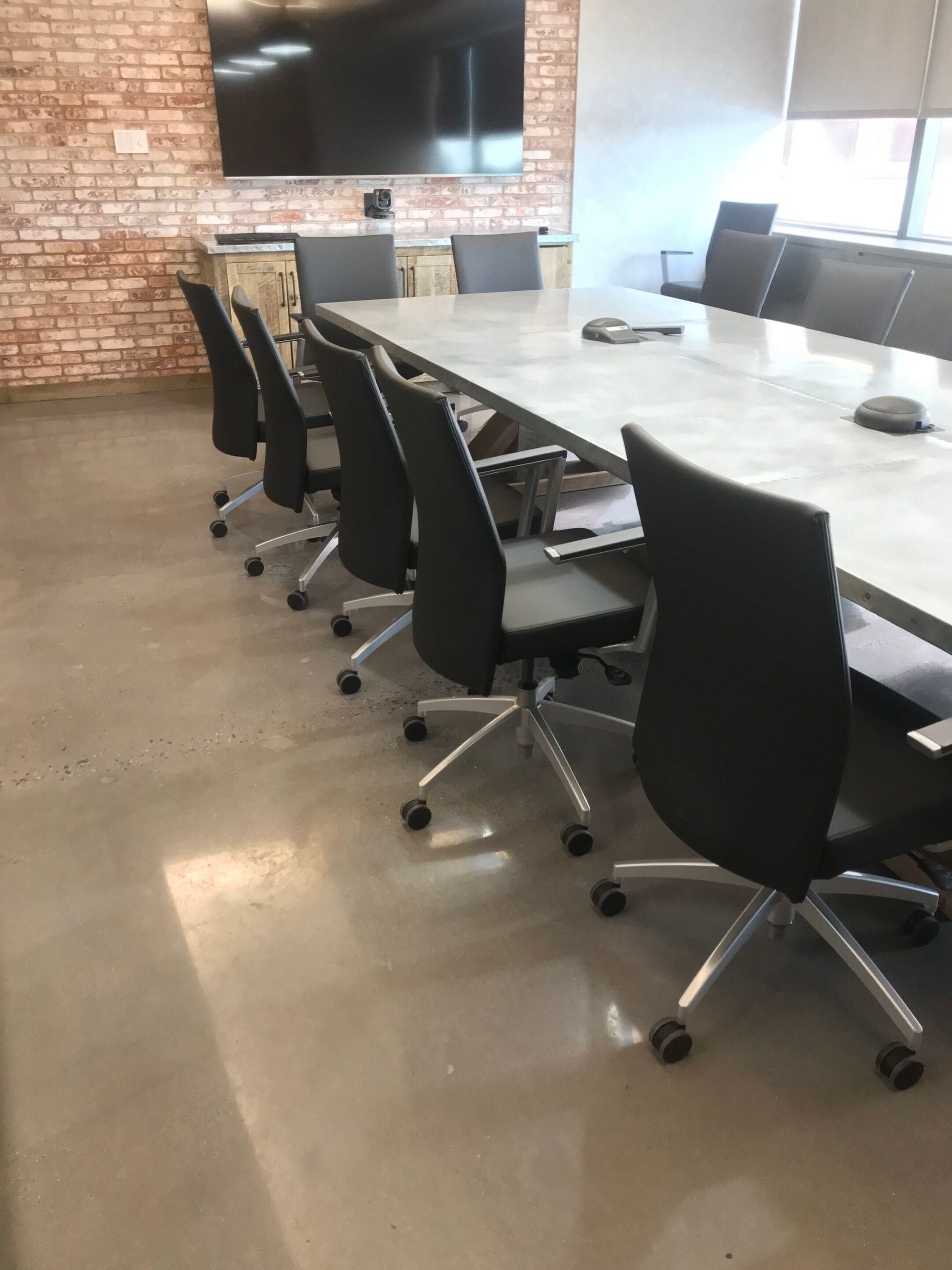 Conference room with black swivel chairs around a long white table and a wall-mounted TV.