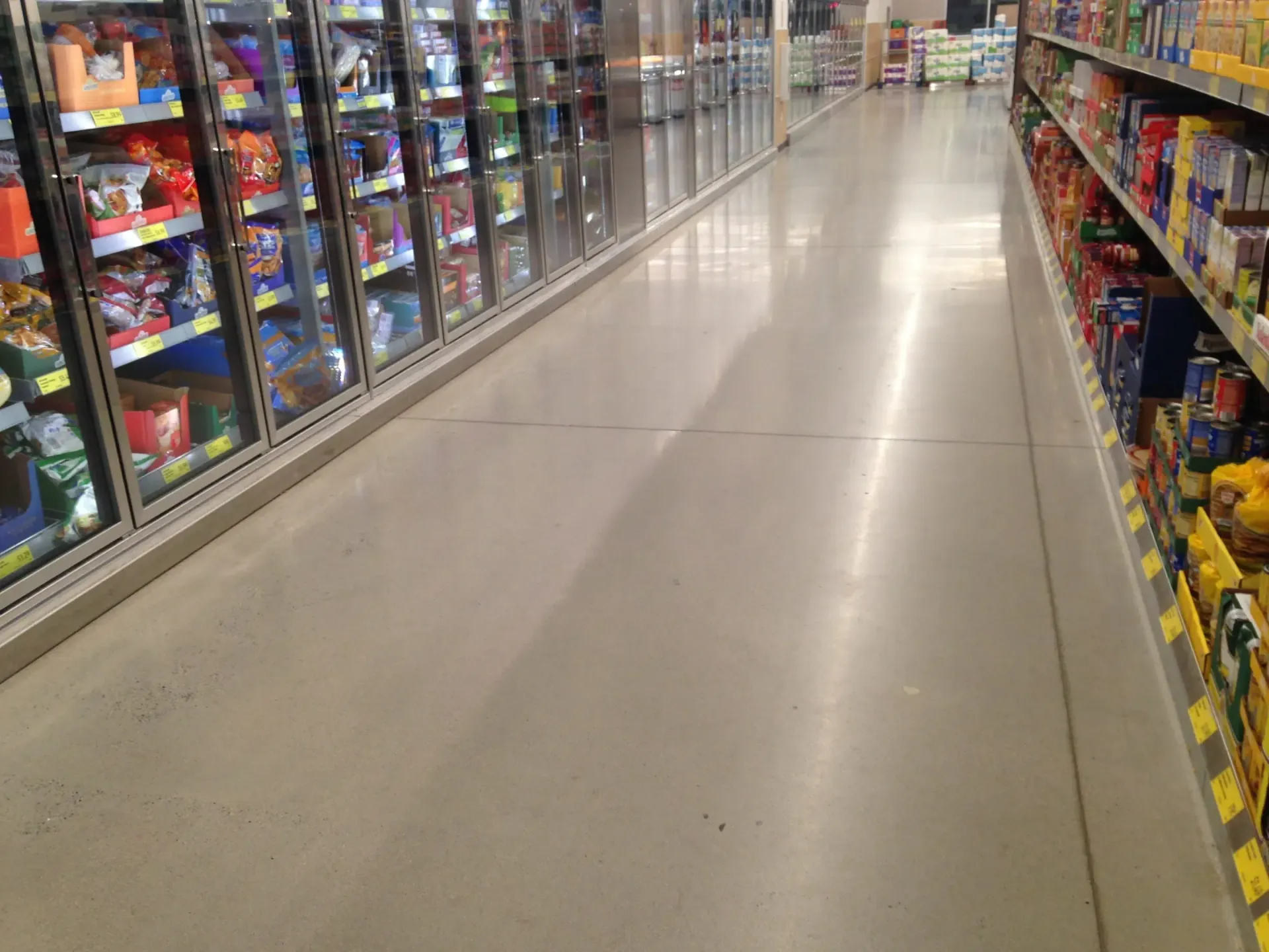 A wide grocery store aisle lined with shelves of colorful products on both sides.