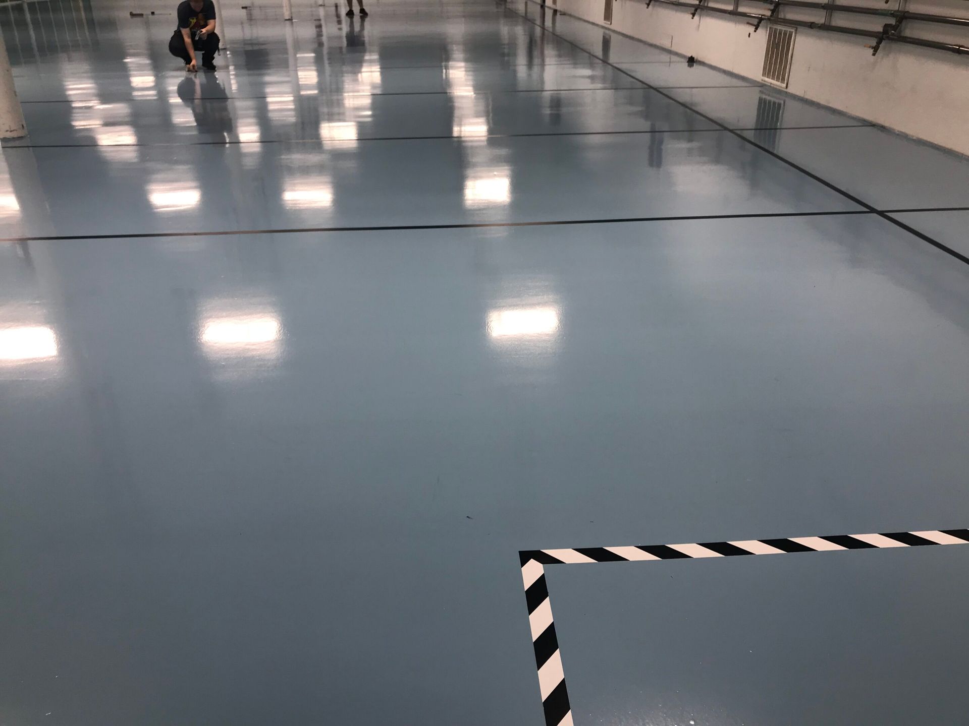 Empty blue indoor floor with a person in the distance and black-and-white striped tape in the foreground