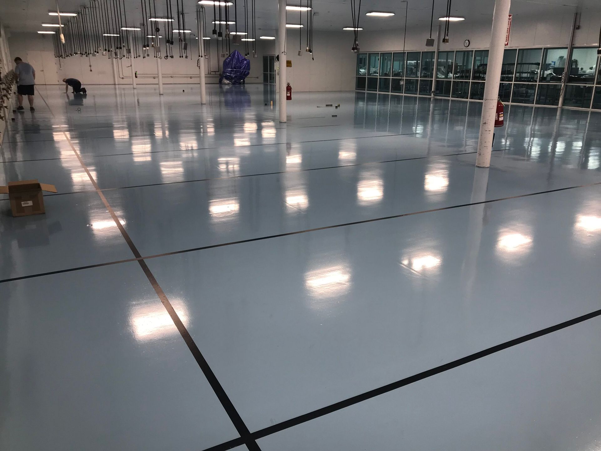 Empty warehouse with glossy floor, overhead lights reflected, and a few workers in the distance