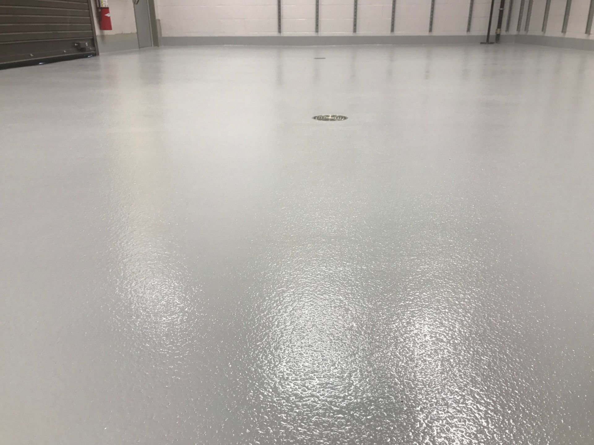 Empty gray warehouse floor with a glossy reflection and closed doors in the background