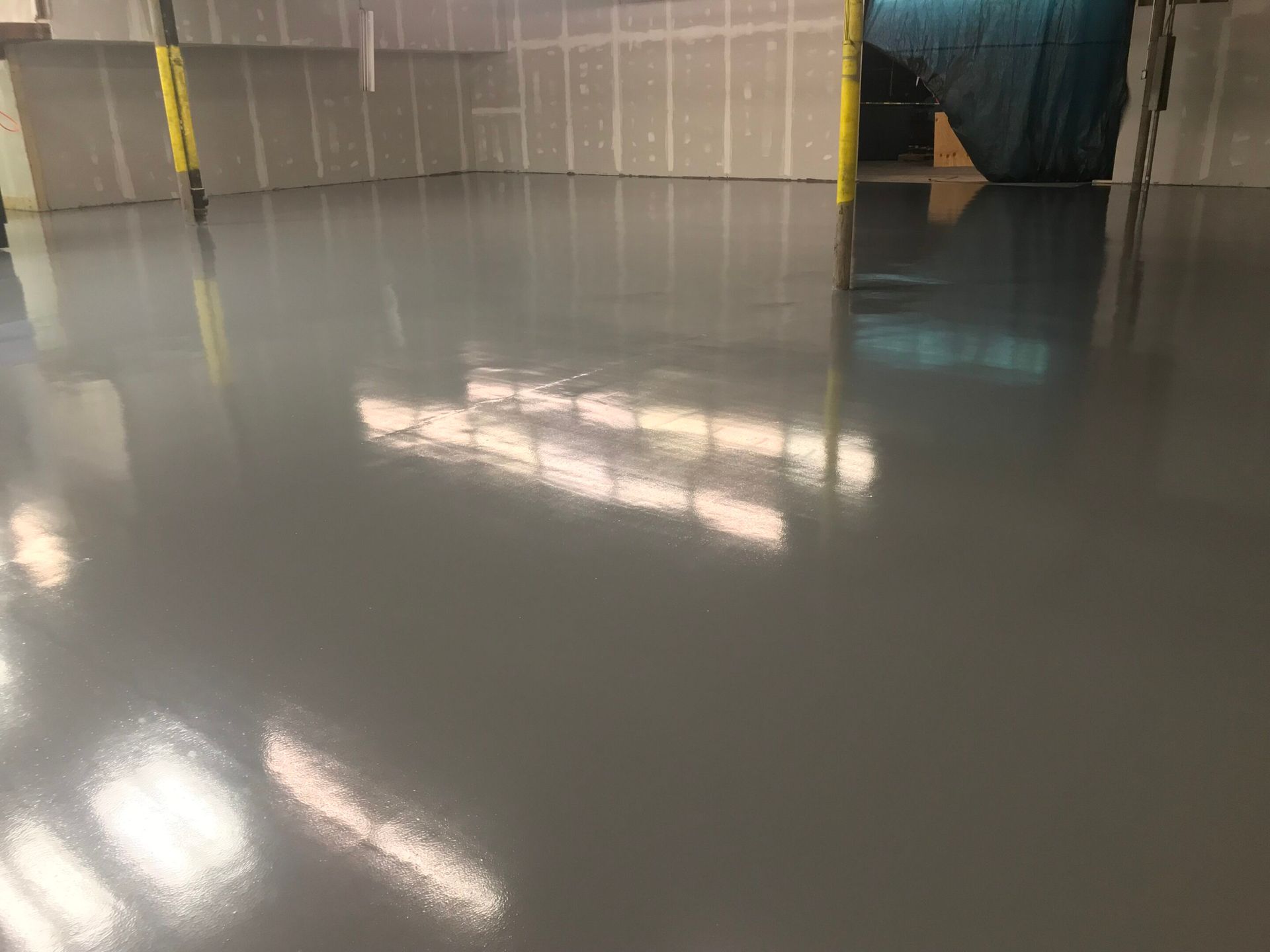 Empty warehouse floor with glossy gray concrete reflecting overhead lights and wall panels