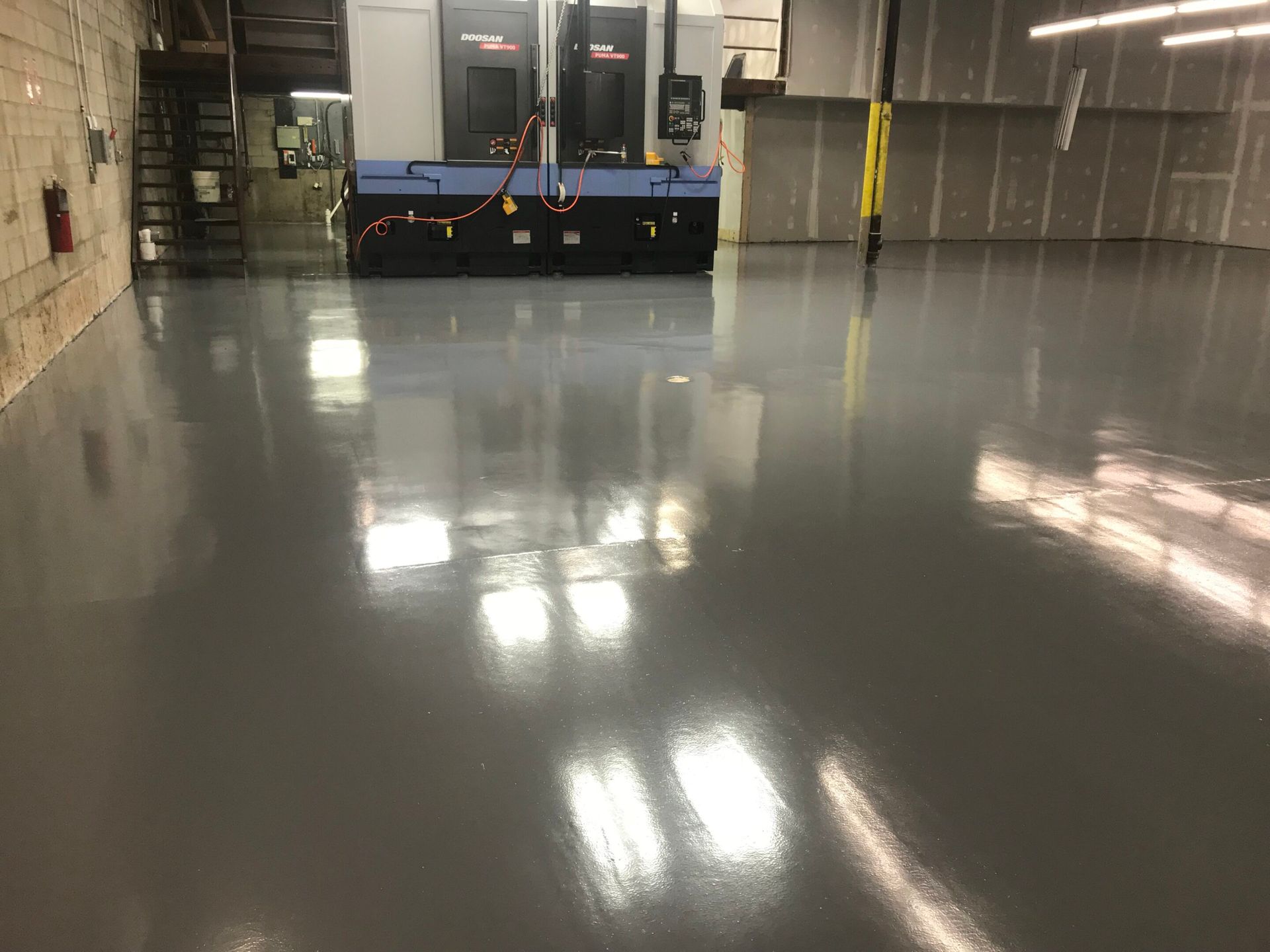 Empty warehouse floor with a polished concrete surface and a blue industrial machine at the far end