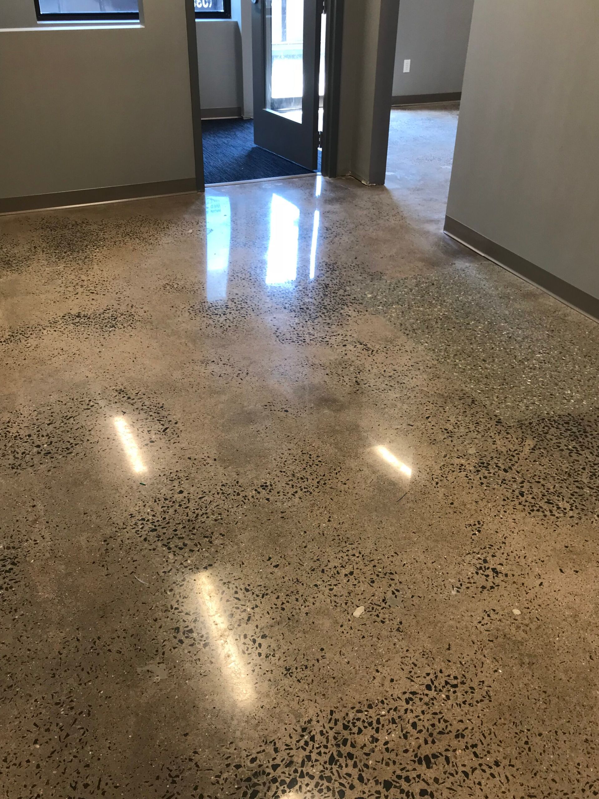 Polished speckled floor in a hallway with open doorways and reflected overhead lights