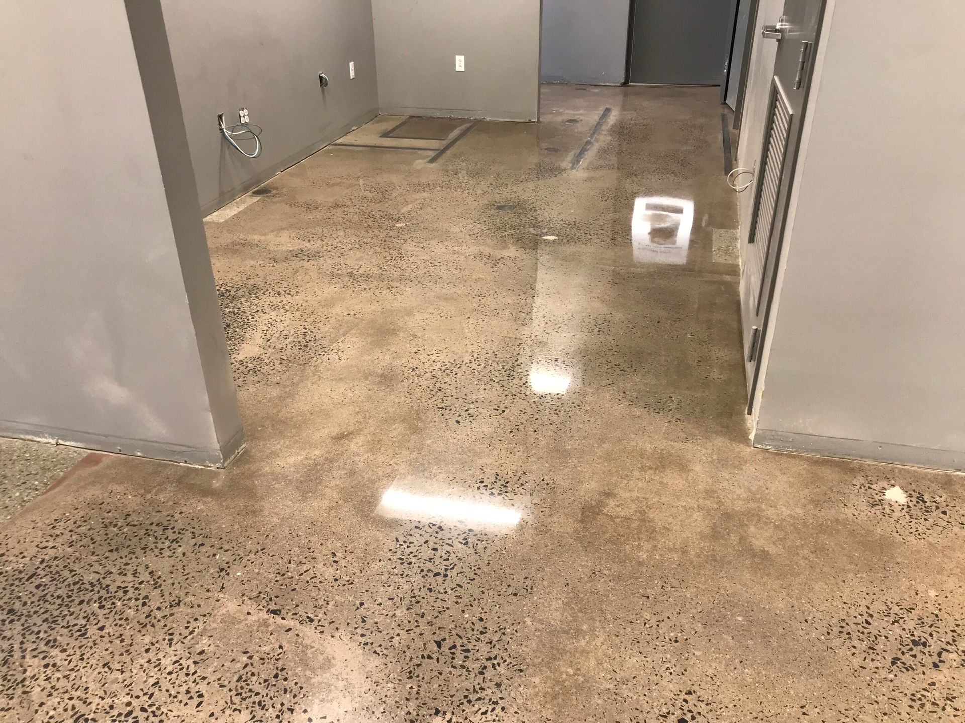 Empty room with glossy speckled concrete floor, gray walls, and a doorway in the back