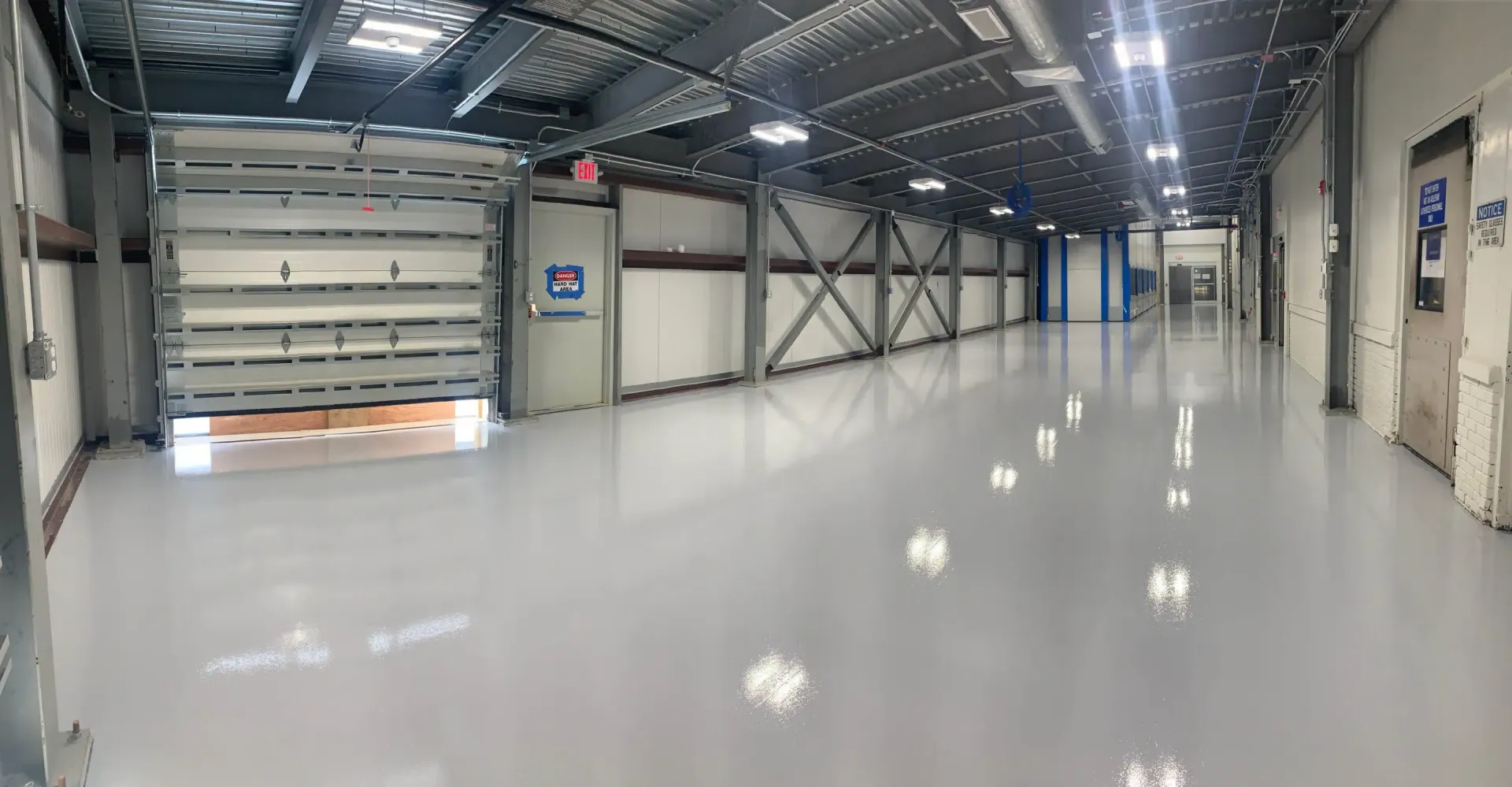 Empty industrial warehouse interior with glossy white floor and overhead lights