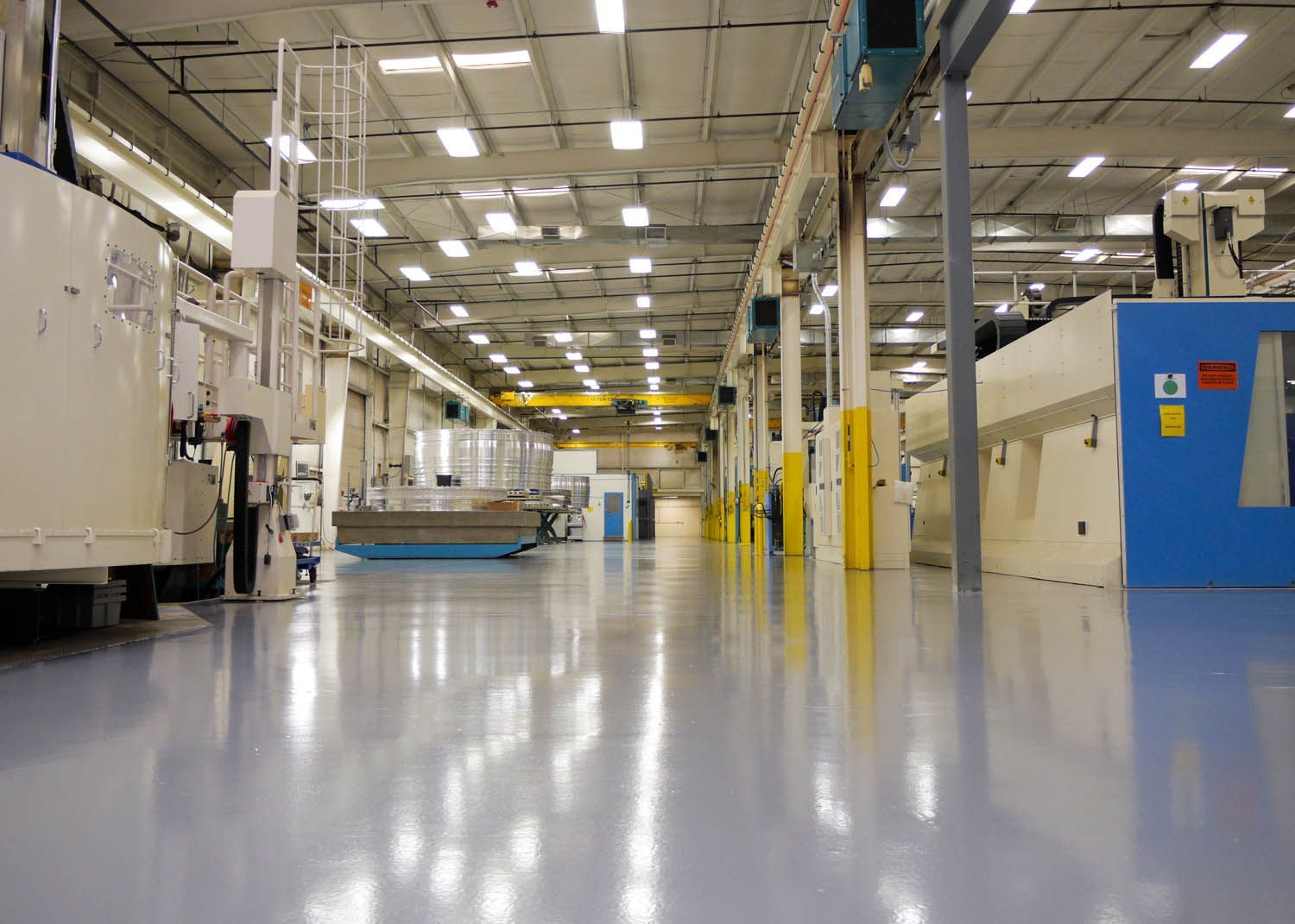 Bright factory interior with polished floor, machinery, and overhead lights in a wide aisle
